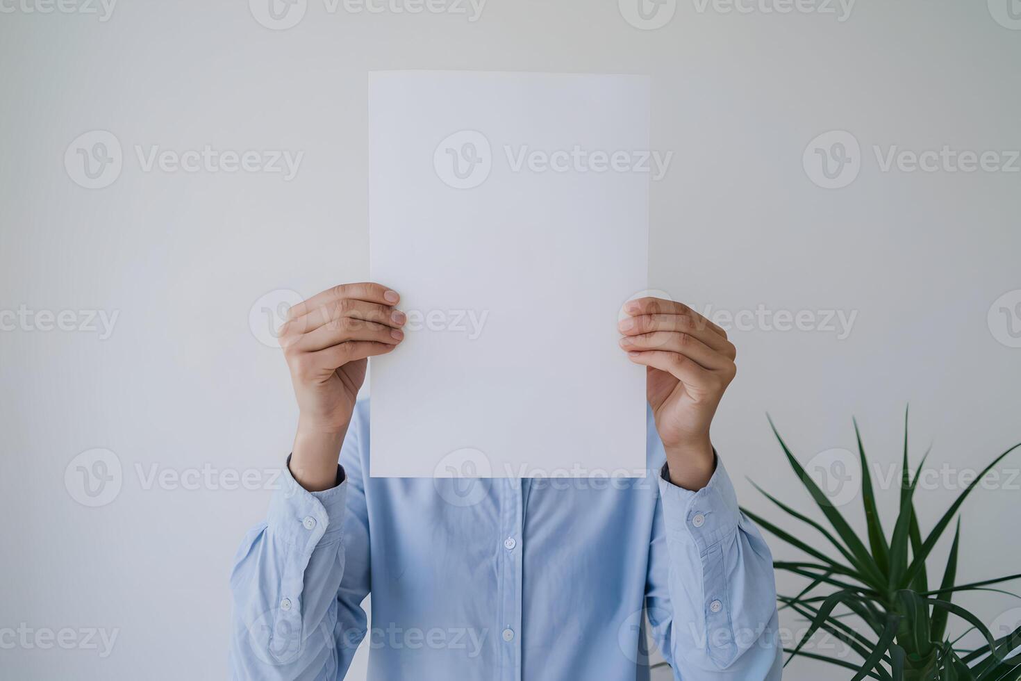 Blank sheet held, obscured face, green plant adds contrast in minimalism photo
