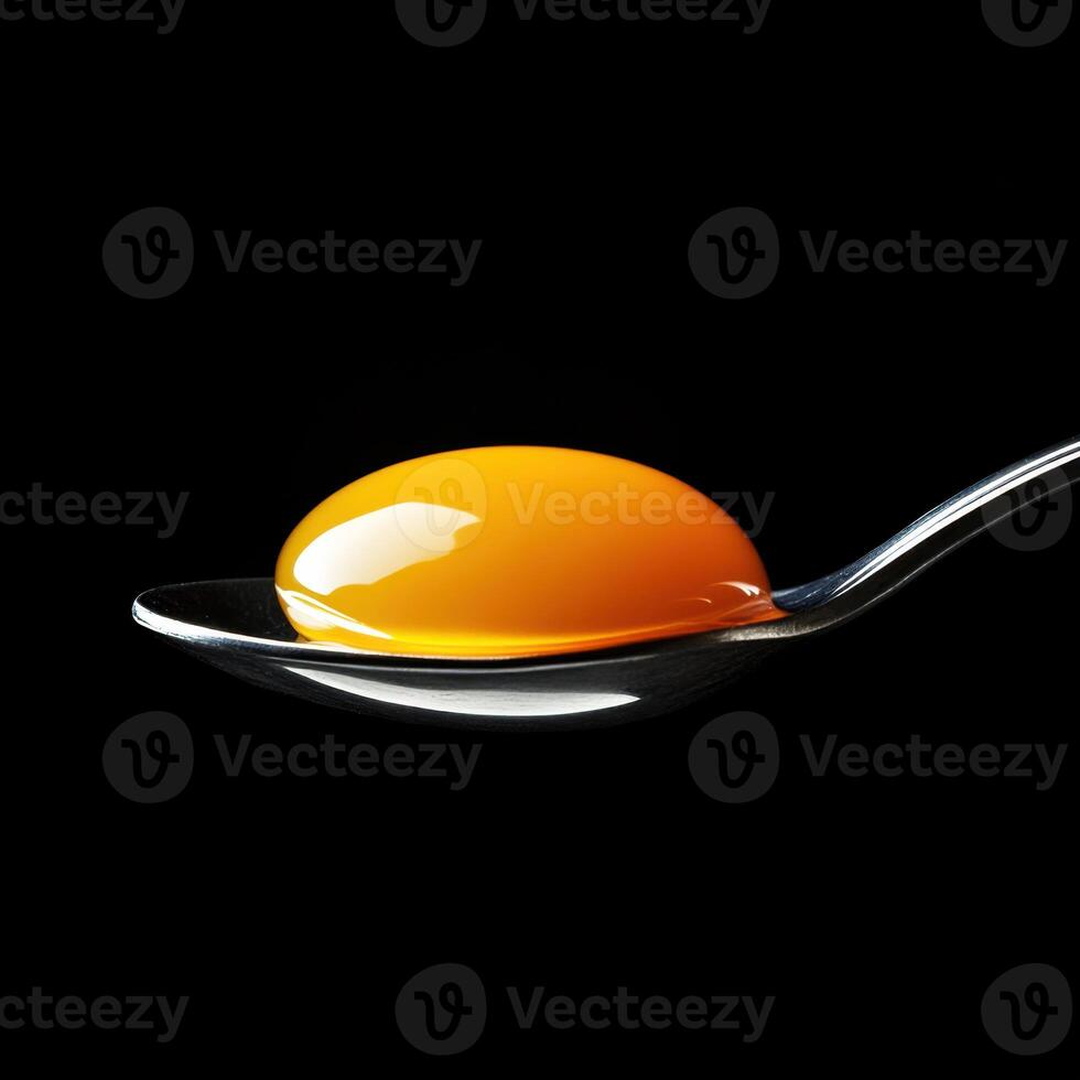 Bright yellow egg yolk resting on a silver spoon against a black background highlighting its texture and color photo