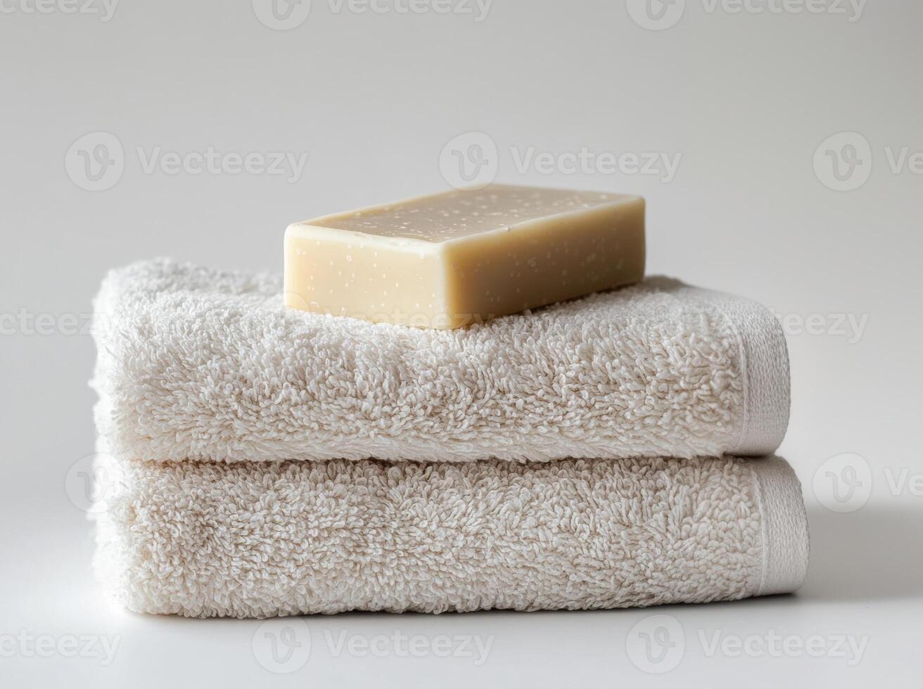 Soft white towels stacked neatly with a bar of soap resting on top in a serene bathroom setting photo