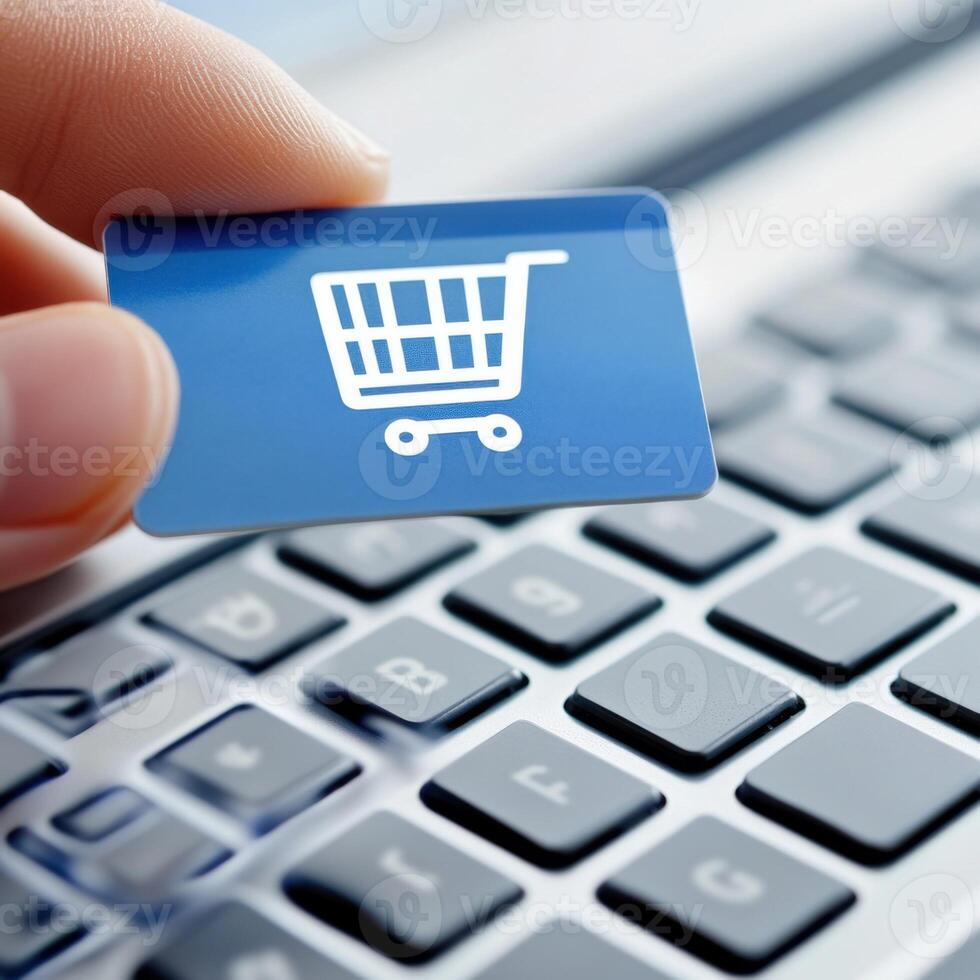 Hand holding a shopping cart card above a laptop keyboard in an online shopping setting photo