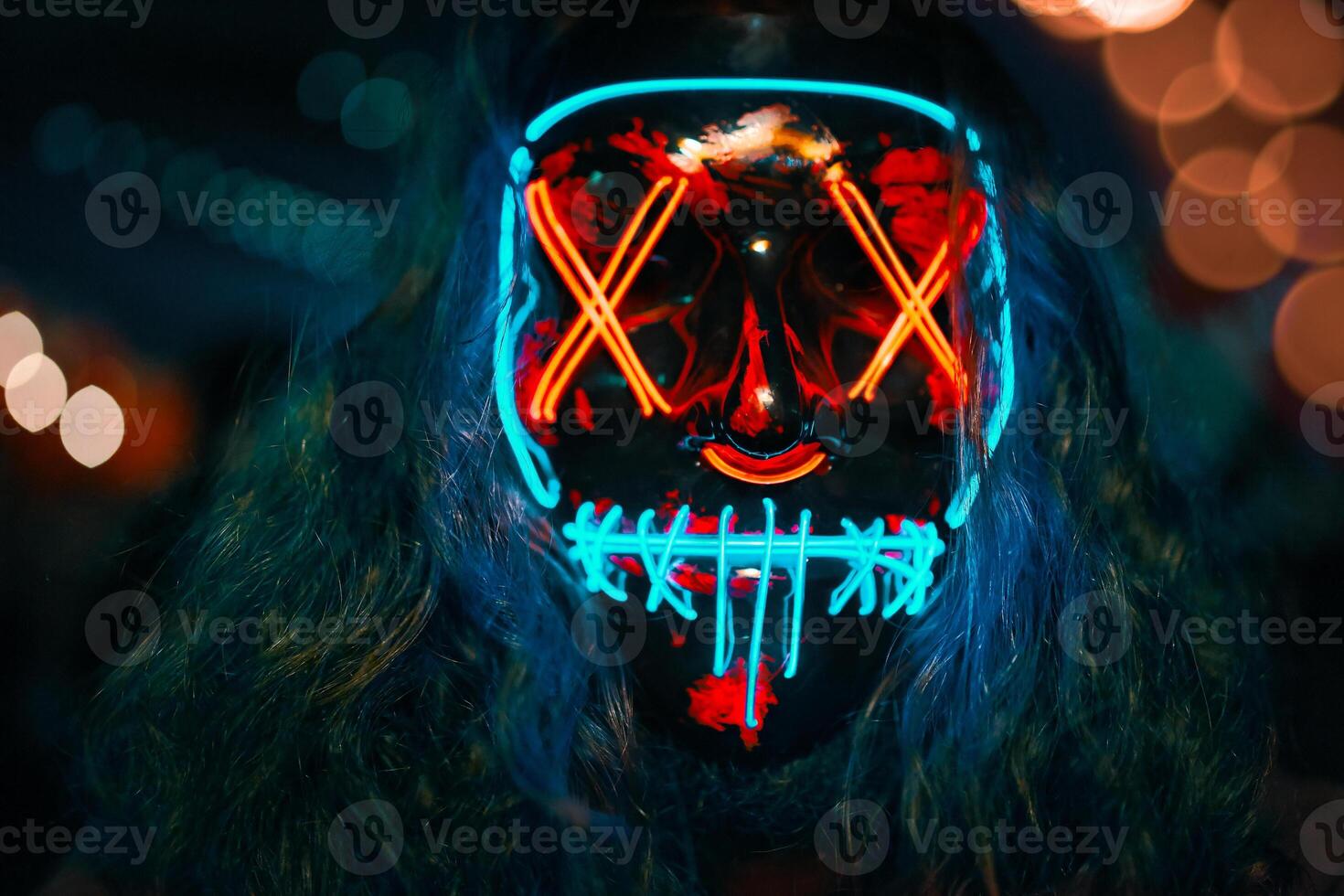 Man with long disheveled hair in a lighting neon glowing mask. Halloween dress-up party. Anonymous person is a cyber criminal. photo