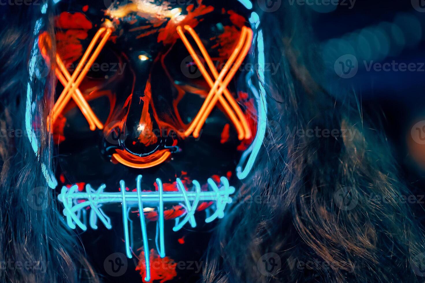 Close up of person with long disheveled hair in a lighting neon glowing mask. Halloween dress-up party in night club. Anonymous person is a cyber criminal. All Saints' Night. photo