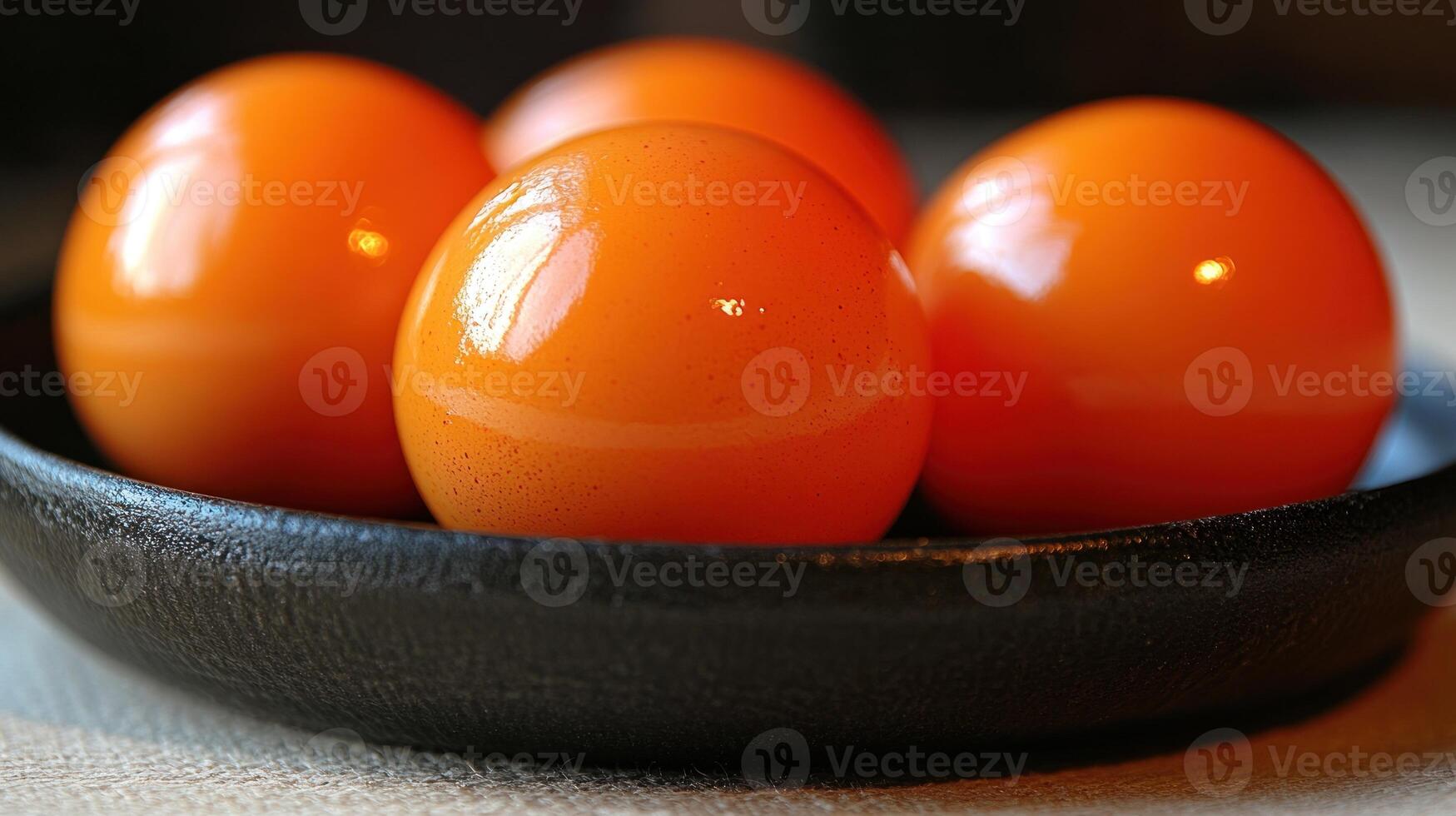 Bright orange spheres in a dark bowl showcase their sheen and invite exploration photo