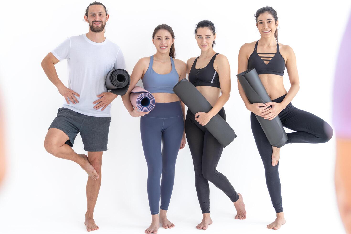 Group of happy sport y women and guy w earing body stylish sportswear holding personal carpets leaned on a white background. waiting for yoga class or body weight class. healthy lifestyle and wellness photo