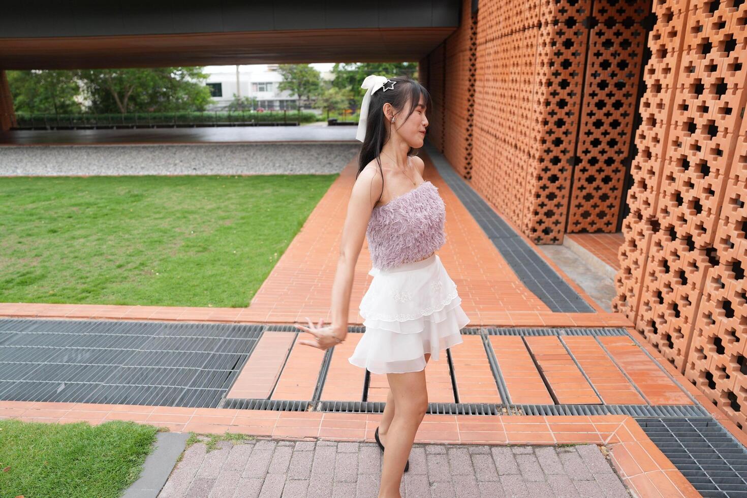 A young woman dances jo yfully in a serene indoor space, framed by a decorative brick wall and lush plants, embodying pure joy. photo