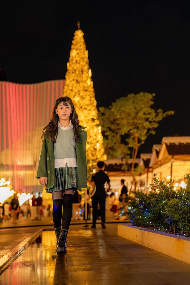 a young girl in a green coat and boots standing in front of a christmas tree photo