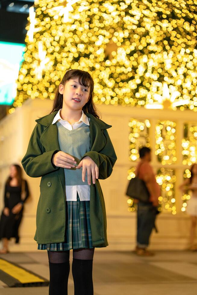 woman outdoors in a green coat, gesturing playfully against a backdrop of golden bokeh lights and a modern building, capturing a lively and festive urban atmosphere photo