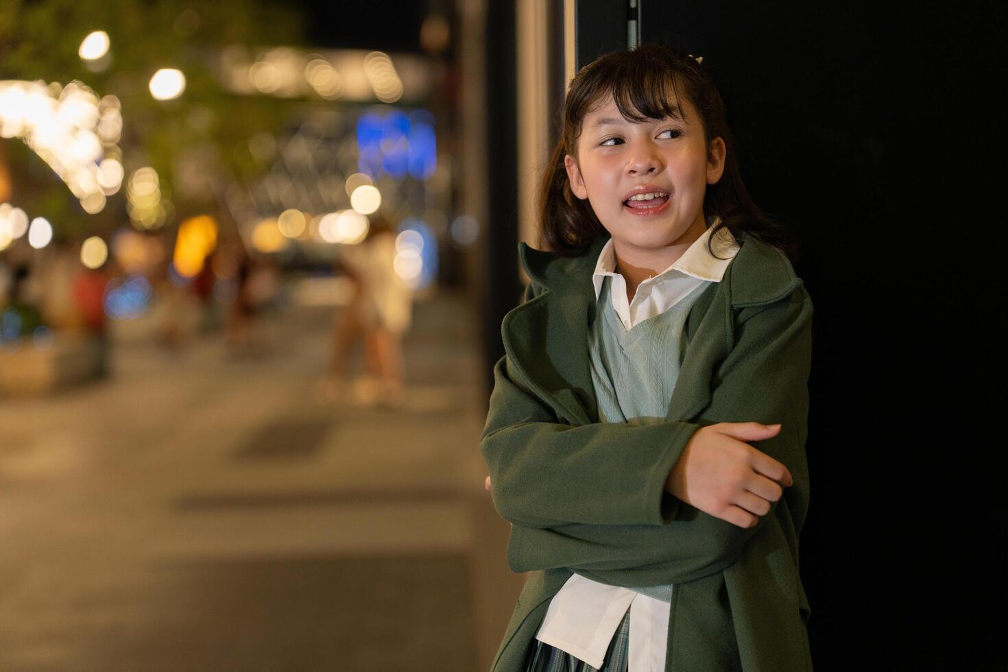 young woman outdoors in a green coat, gesturing playfully against a backdrop of golden bokeh lights and a modern building, capturing a lively and festive urban atmosphere. photo