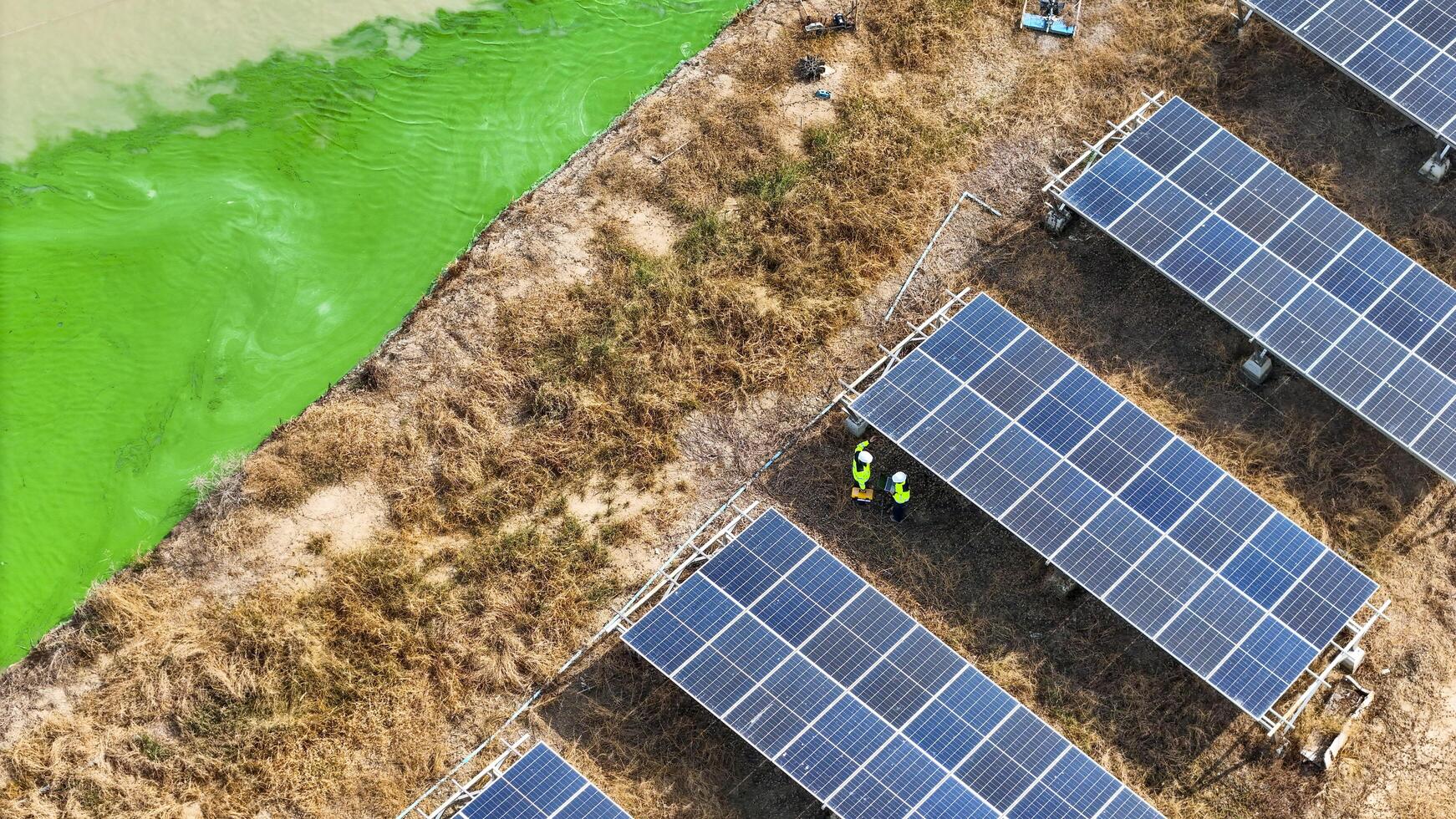Top view of solar arrays with a bright g reen waterbody and technicians, representing progress in renewable energy and the harmony between modern technology and environmental conservation. photo