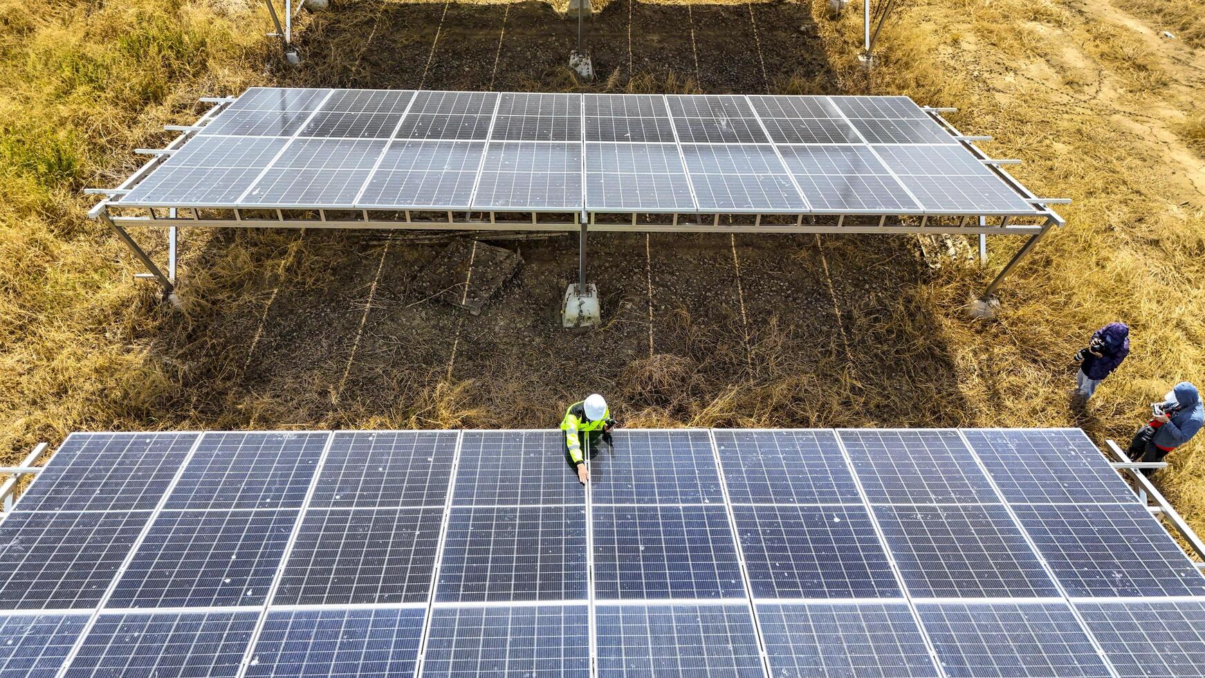 Two workers in safety gear performing maintenance under solar panels in a field, h ighlighting renewable energy, sustainability, and the efficient management of solar power systems in natural settings photo
