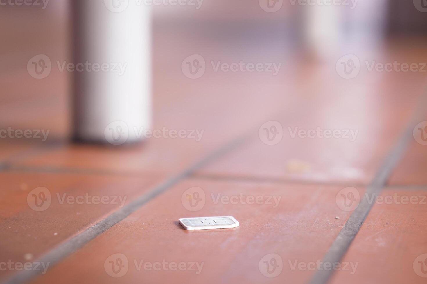 a phone sim card dropped on a tiles floor. lost sim card concept photo