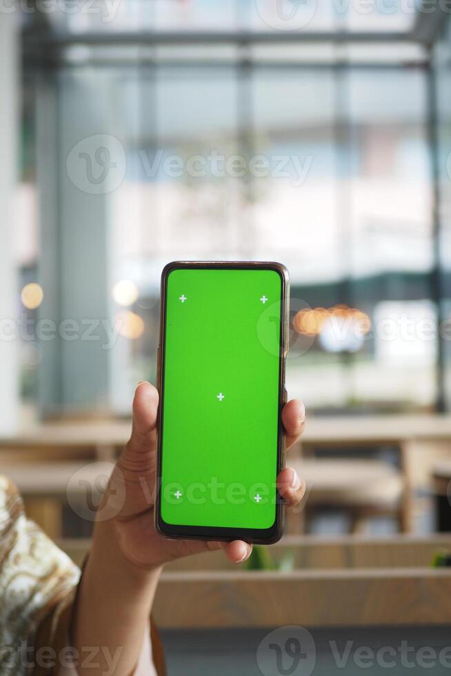 A person with a smartphone on a green screen sits in a cafe photo