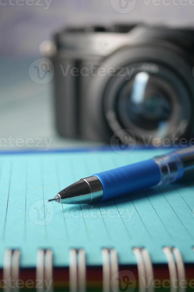 Close-up of a Pen on a Notebook with a Camera in the Background photo
