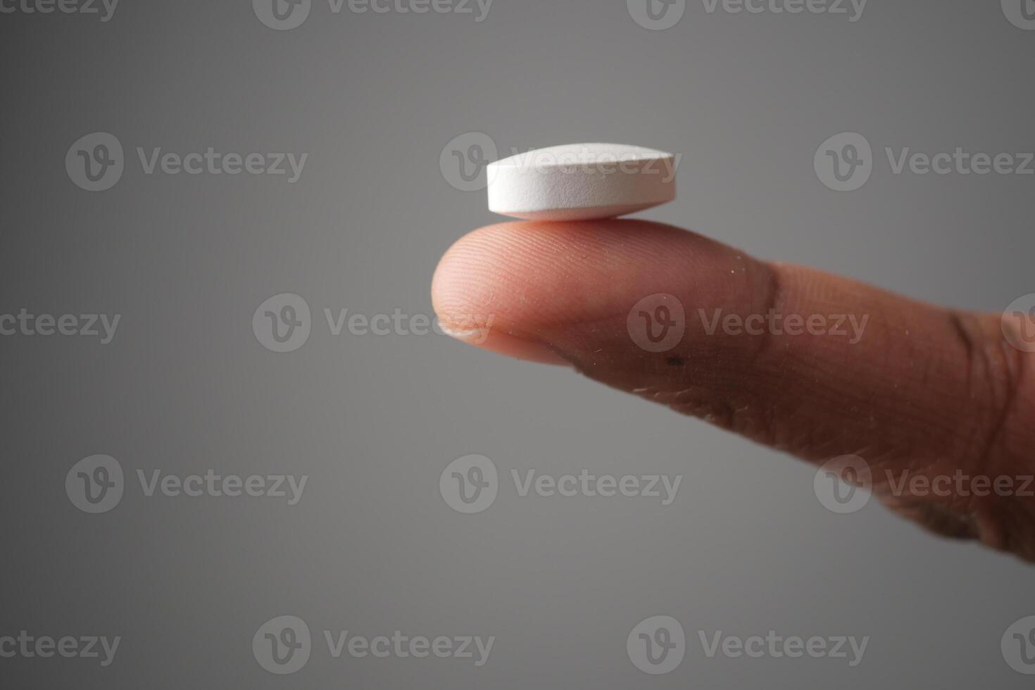 A detailed closeup image of a White Pill delicately Balanced on a Finger photo