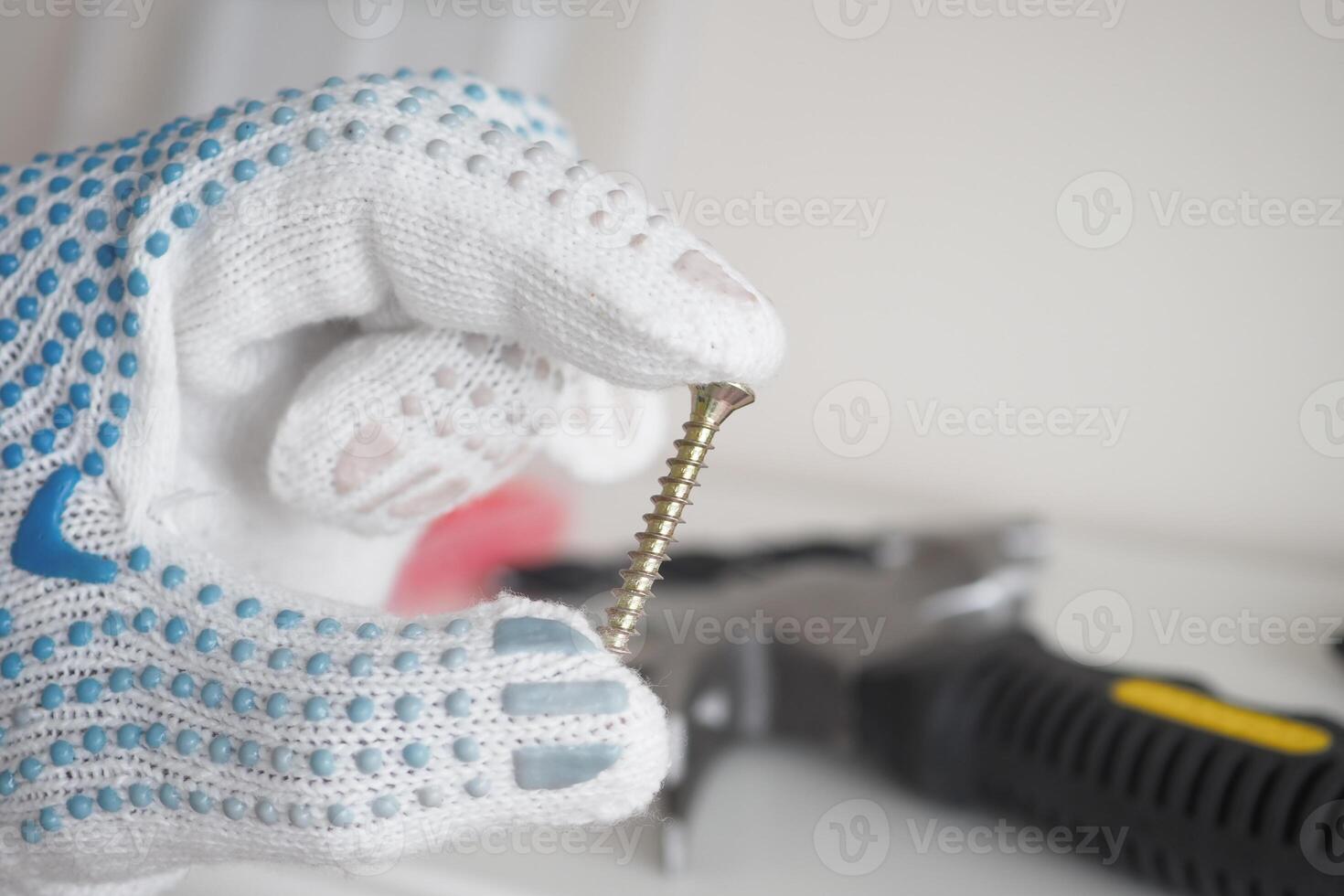 A hand gripping a screw while wearing safety gloves in a workshop setting photo