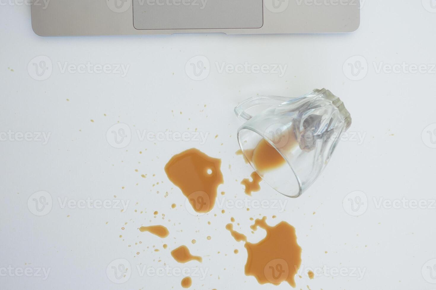 A drink was accidentally spilled on a desk with a laptop and glasses, creating a mess photo