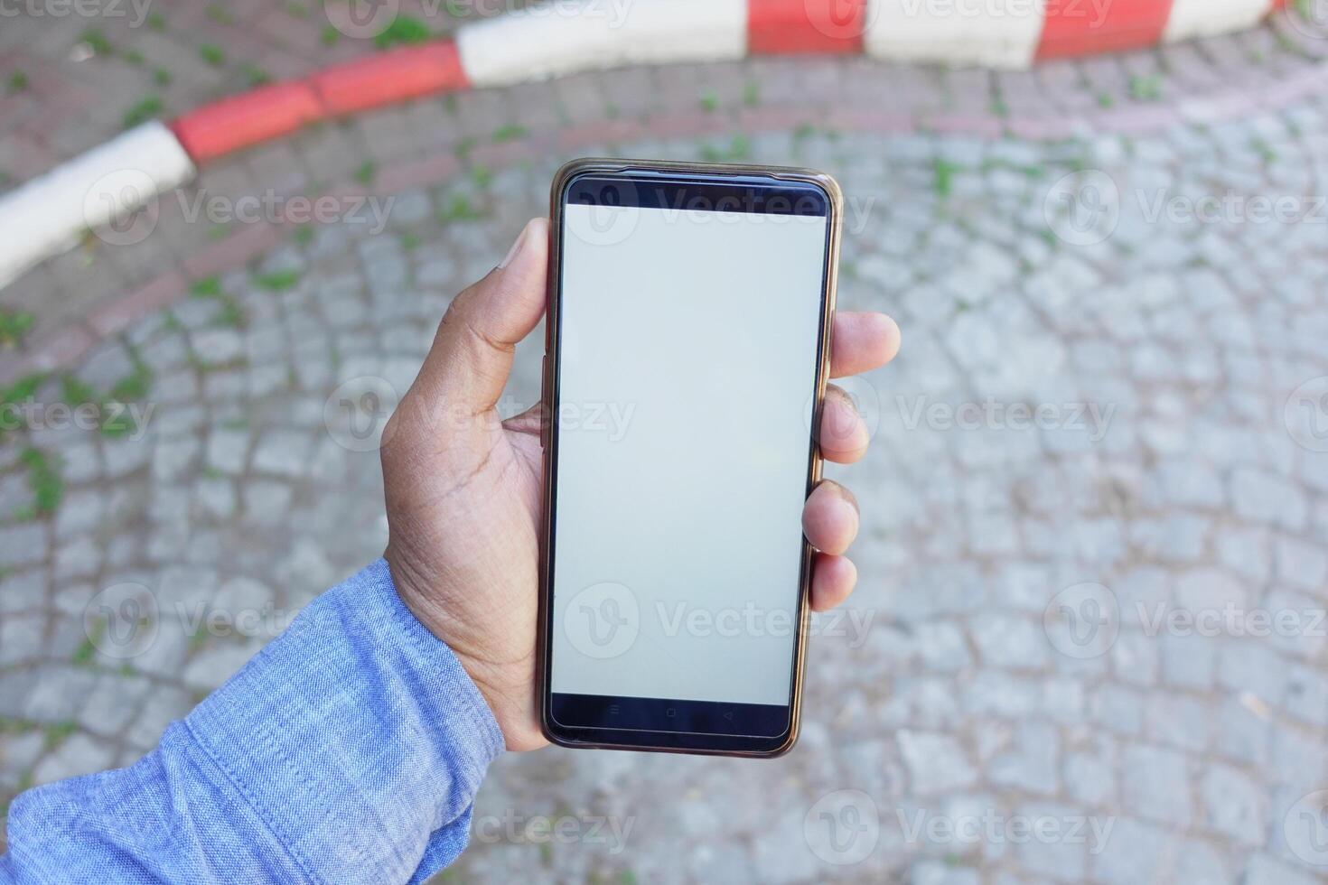 A person is holding a smartphone that has a blank screen while outdoors photo