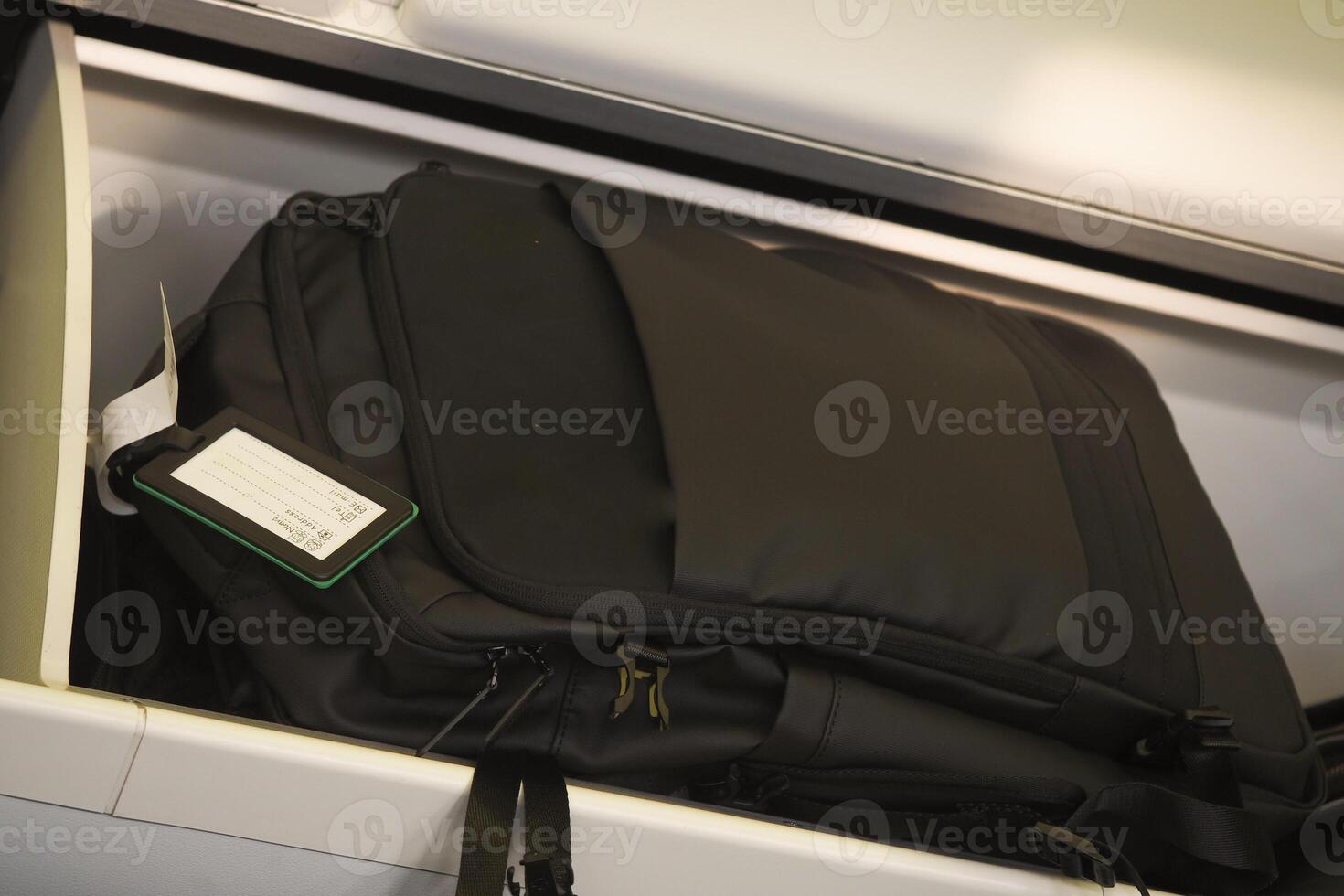 A black backpack has been conveniently stored in the overhead cabin space photo