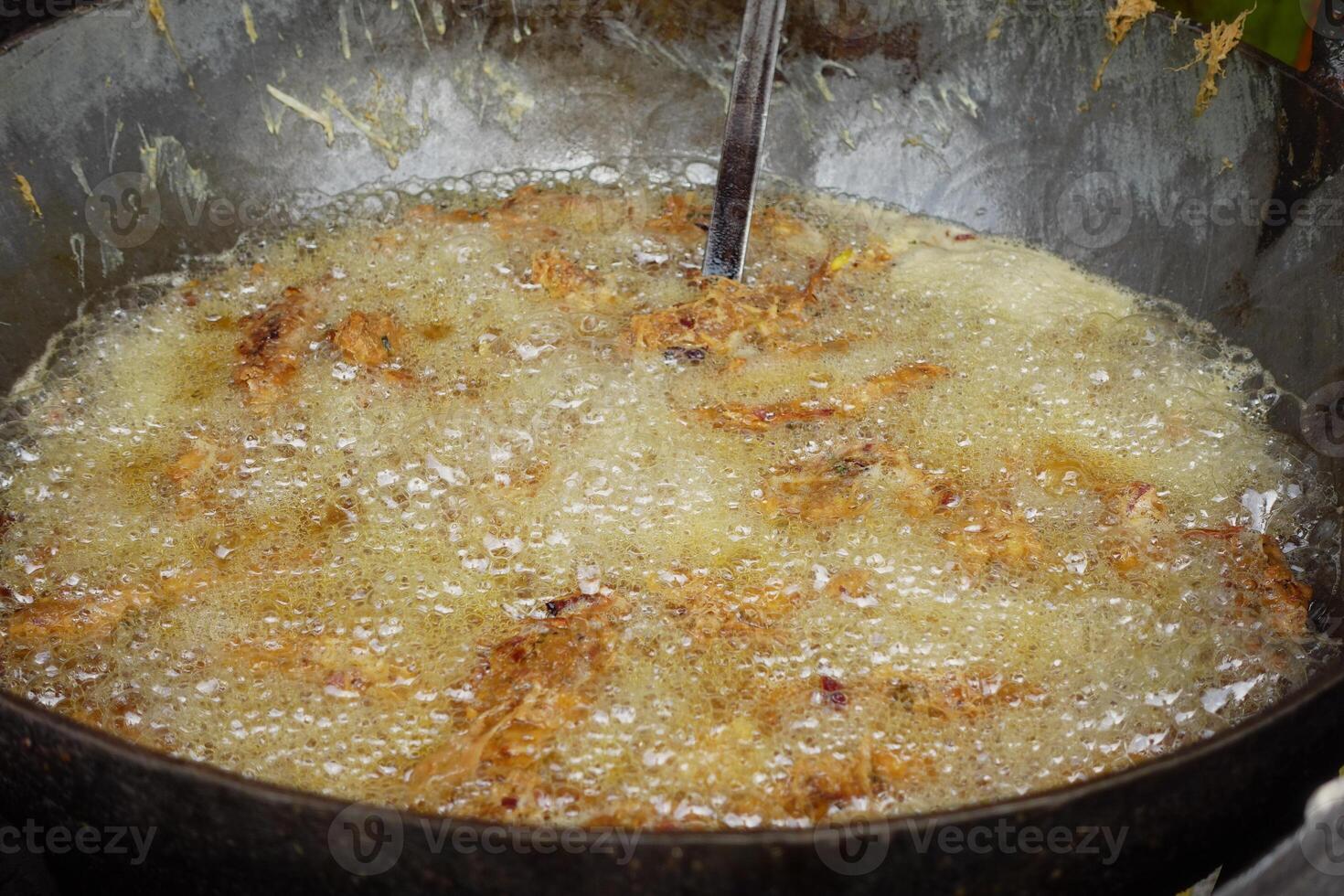 Delicious golden crispy food is frying in a large pan filled with hot bubbling oil, photo