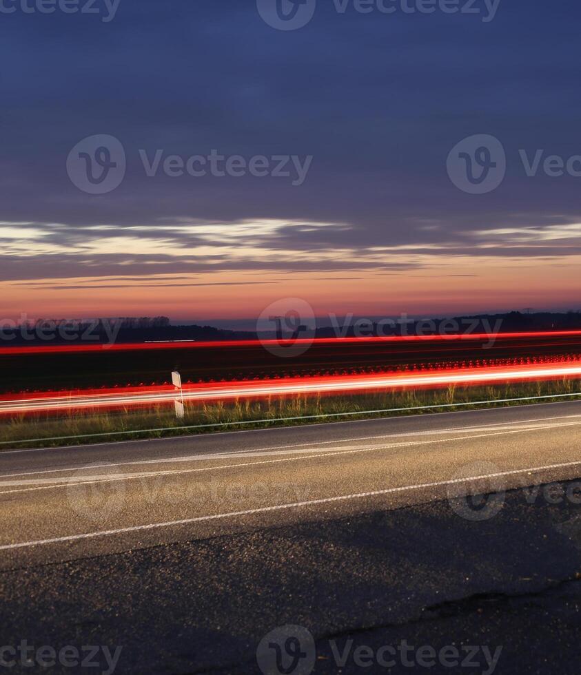 Sunset over a federal road - Bundesstrasse - near Greifswald, Mecklenburg-Vorpommern, Germany. Long exposure makes the movement of car lights and clouds visible. photo