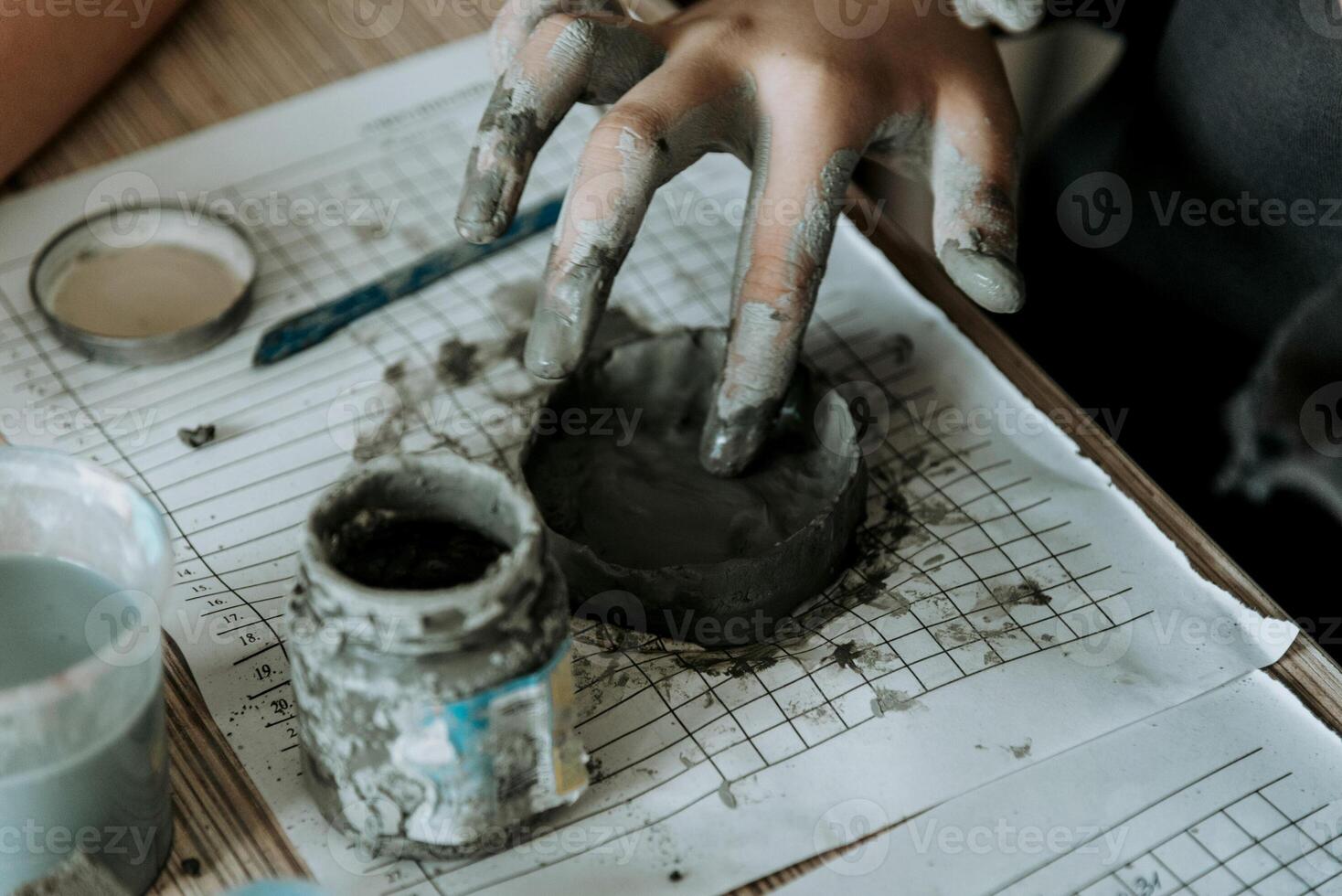 Potter nice sculpts mug from clay, close up dirty hands create vase on white paper photo