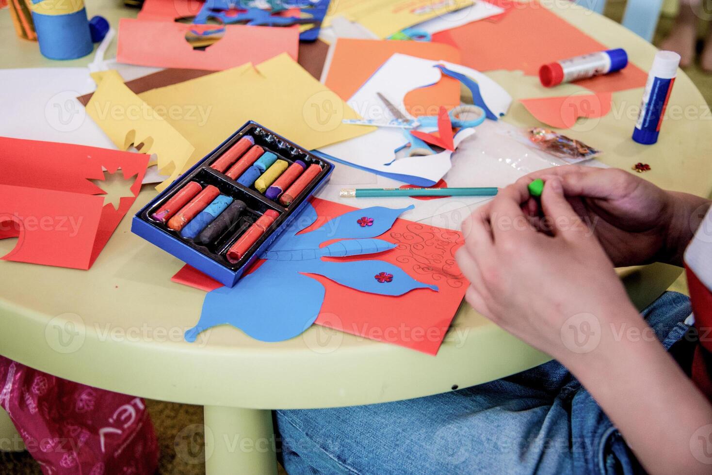 Child makes craft from colored paper, kid lovely draw kindergarten, preschool education photo