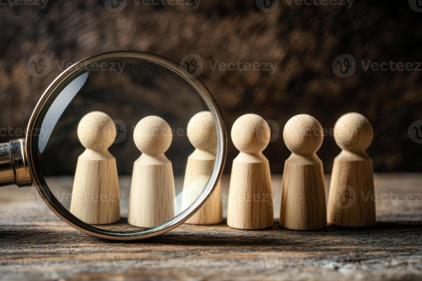 A magnifying glass distinctly highlights wooden figures, effectively symbolizing both the concept of scrutiny and the ongoing search for individuals hidden within a larger group or collective setting photo