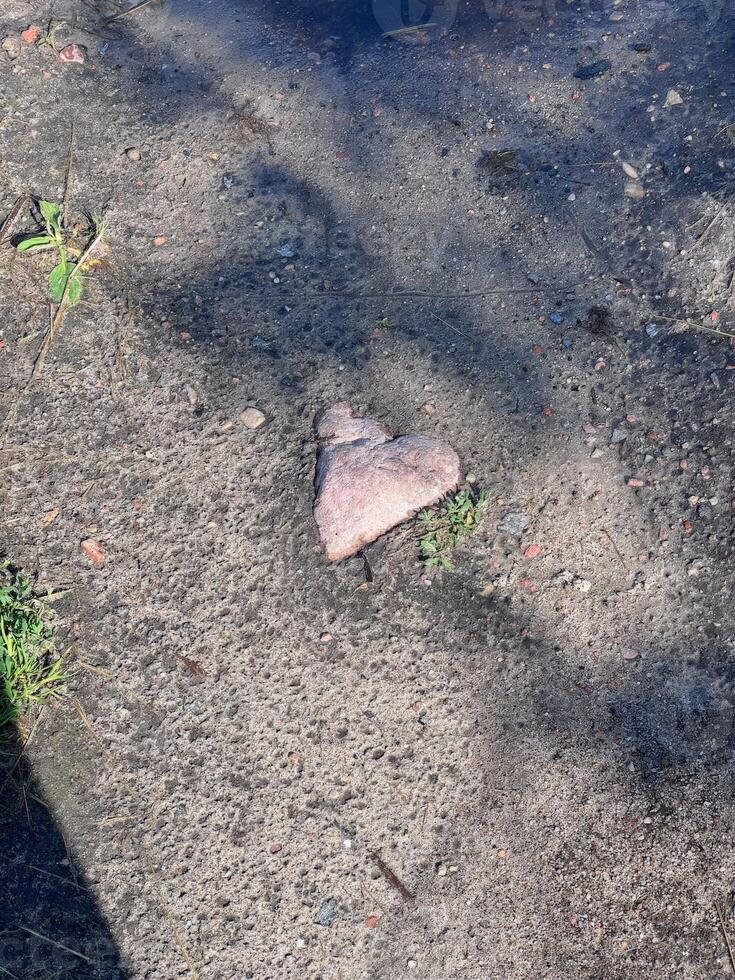 A heart-shaped rock rests on a concrete surface, partially surrounded by grass and dirt, cleverly blending natural beauty with urban settings, inviting curiosity photo