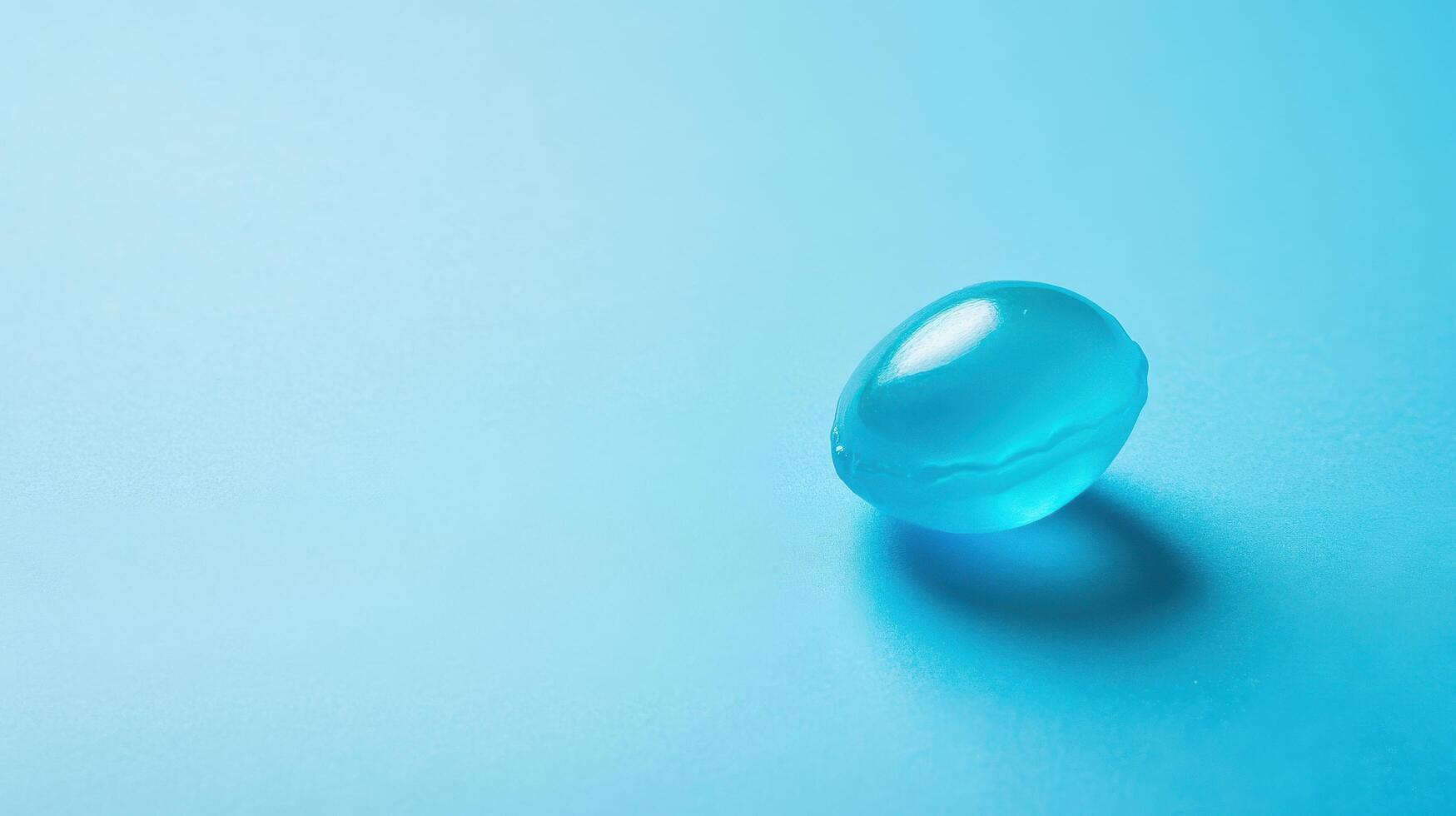 Blue gel capsule resting on a textured aqua surface under soft lighting photo