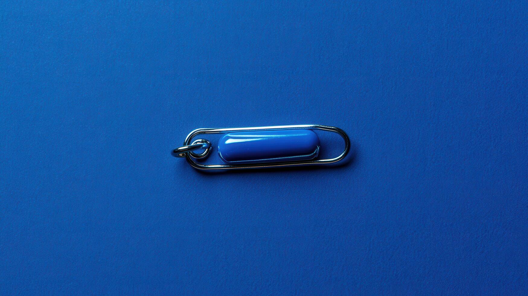 Blue safety pin placed on a vibrant blue background highlighting its design and color contrast photo