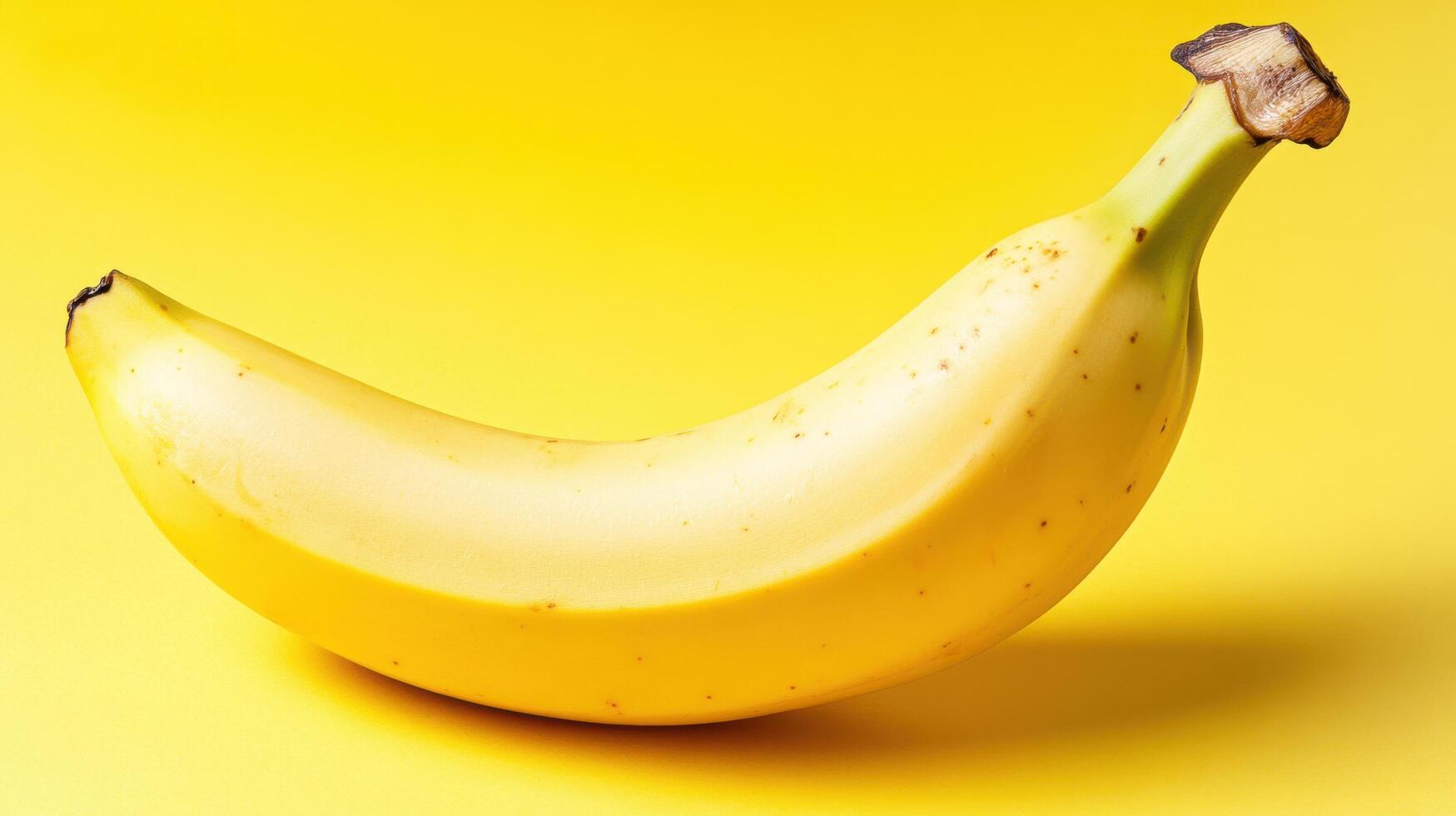 Yellow banana resting on bright yellow background, showcasing its curved shape and natural speckled texture photo