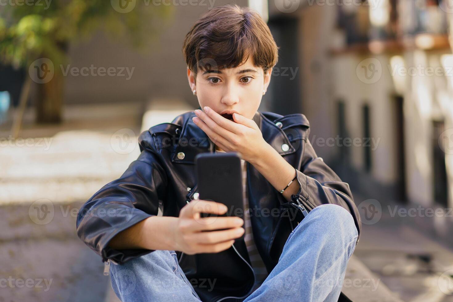 A surprised young individual engaging deeply with their smartphone while sitting on urban steps photo