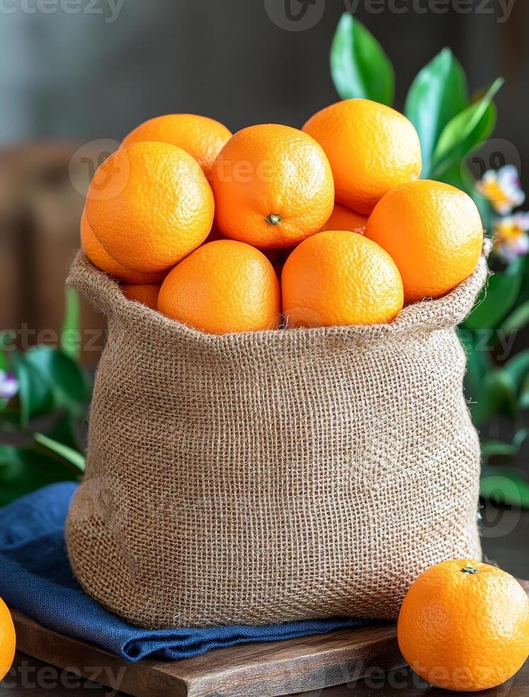 Oranges in a burlap sack. Freshly harvested oranges in a burlap sack displayed on a wooden table with green leaves and a blue cloth photo