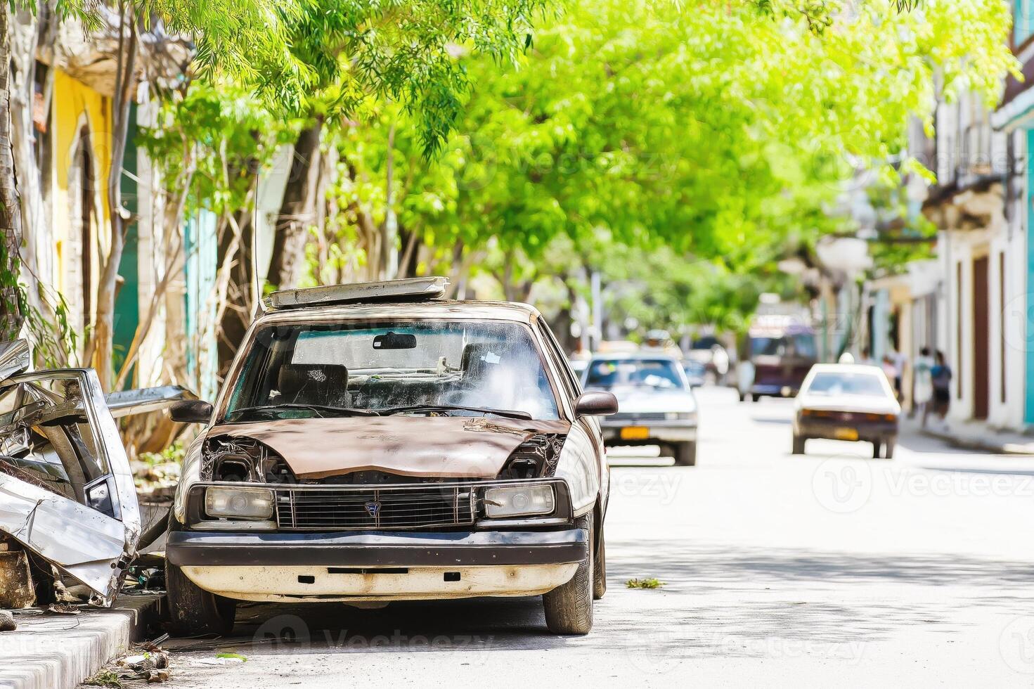 Old car resting on a tranquil street in Cuba amidst faded colors and lush greenery reflecting the charm of a bygone era photo