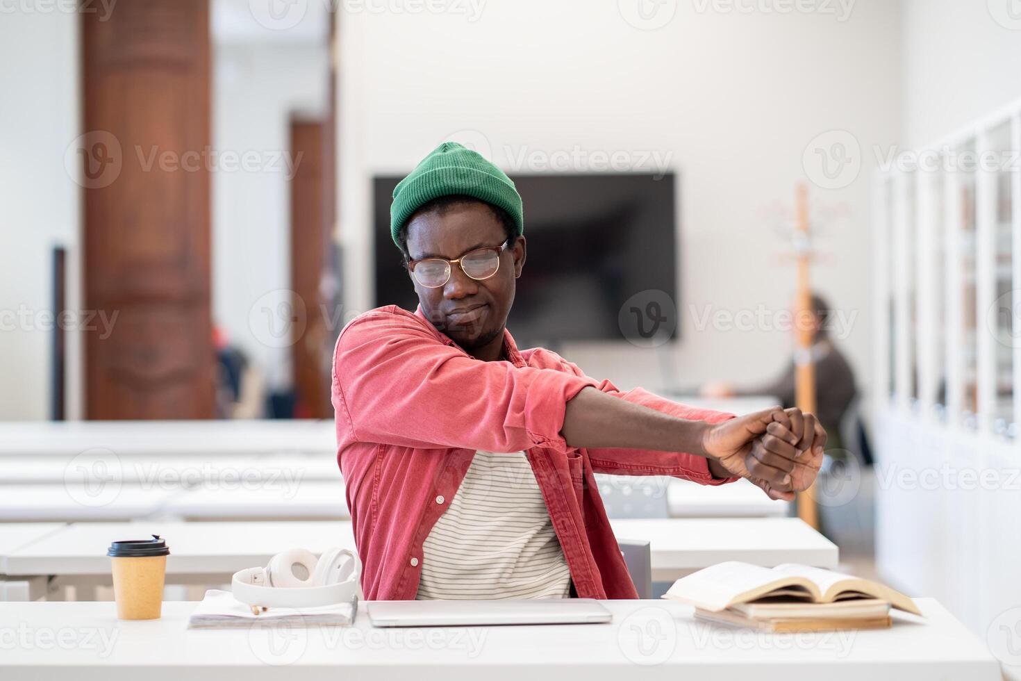 TIred African student guy stretching hands, relaxing mind and muscles after intense study in library photo