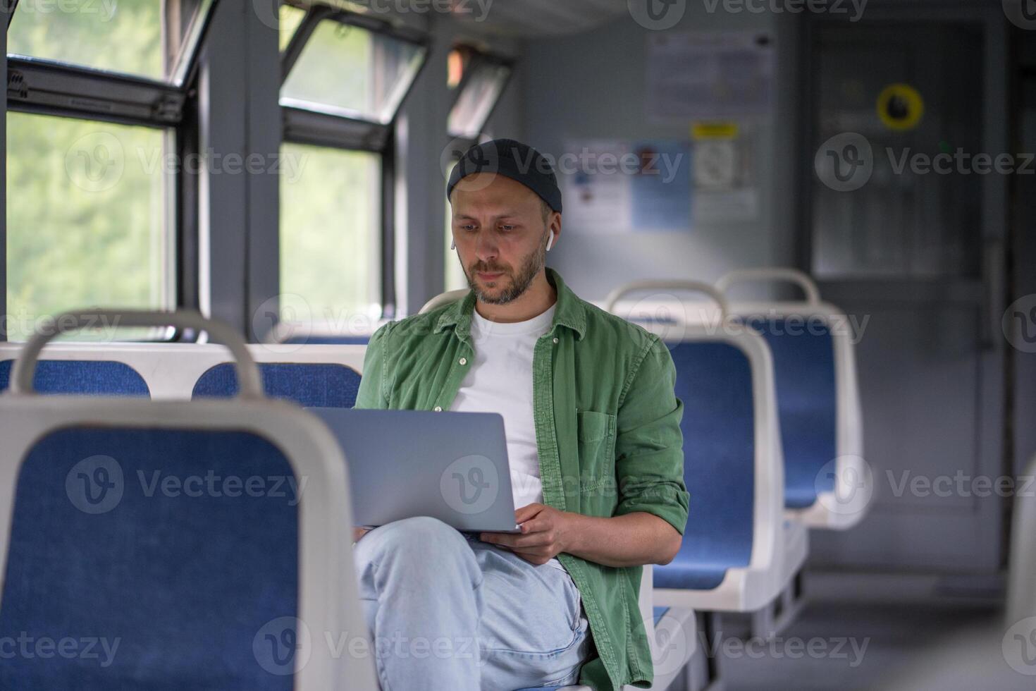 Focused thoughtful man passenger working on laptop while travel by electric train using earphones photo
