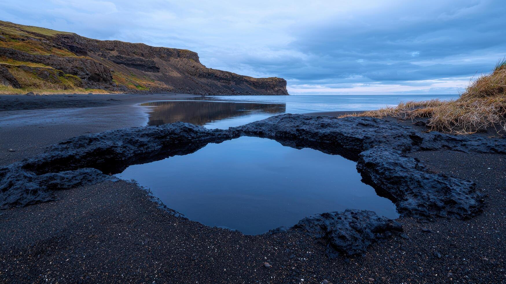 Tide pool on a black sand beach with cliffs in the background photo