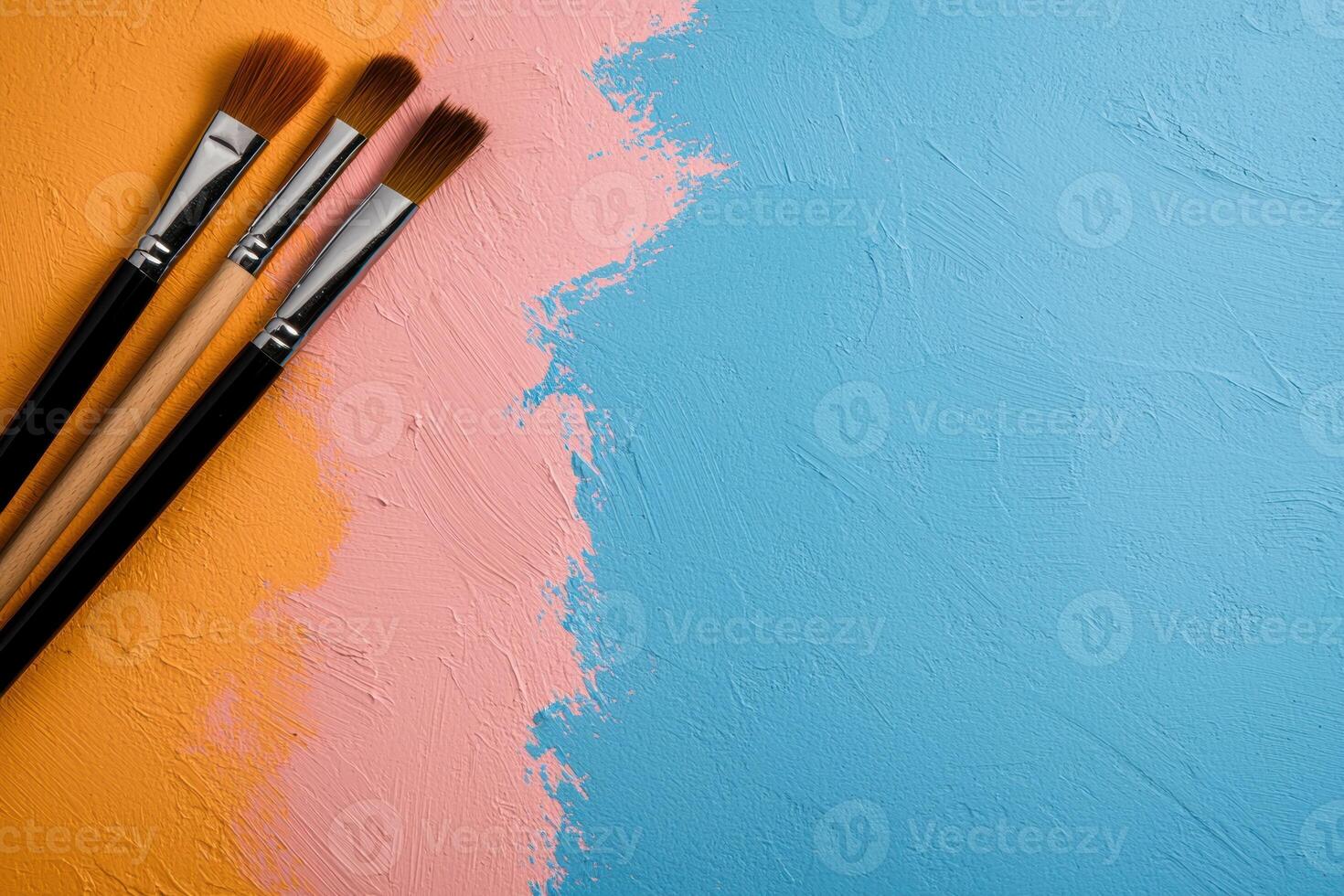 Three paint brushes on a pastel orange, pink and blue painted background photo