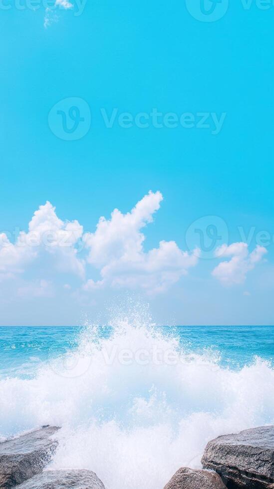 Ocean Waves Crashing Against Stones Under Clear Blue Sky with Fluffy Clouds photo