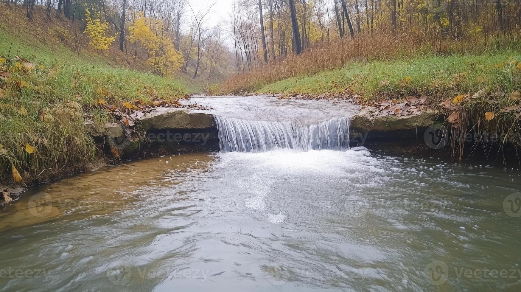 Small Waterfall in Forest on Autumn Day Capturing Tranquil Nature with Flowing Stream, Trees, Green Grass, and Fall Leaves in AR 169 Style Photography Scene for Seasonal Landscape Design photo