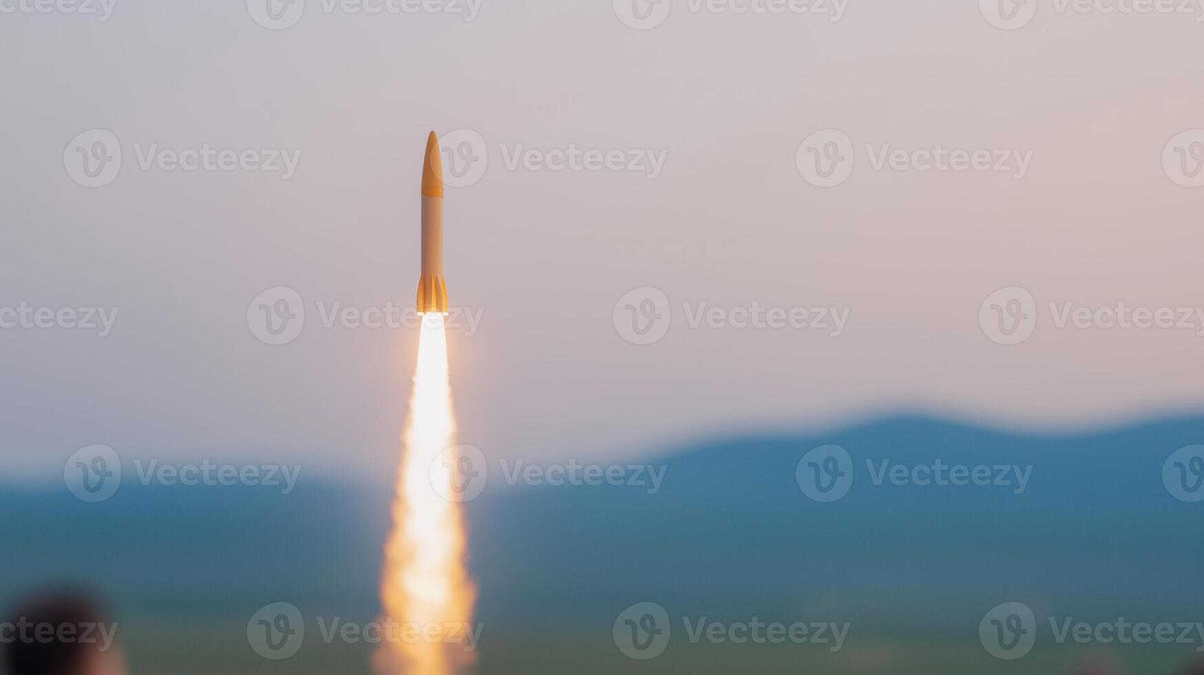 Rocket Launch Against Mountainous Horizon Capturing World Space Week Celebration in Evening Sky Featuring Blurred Foreground and Vivid Contrail Inspiring Exploration with Atmospheric Lighting photo