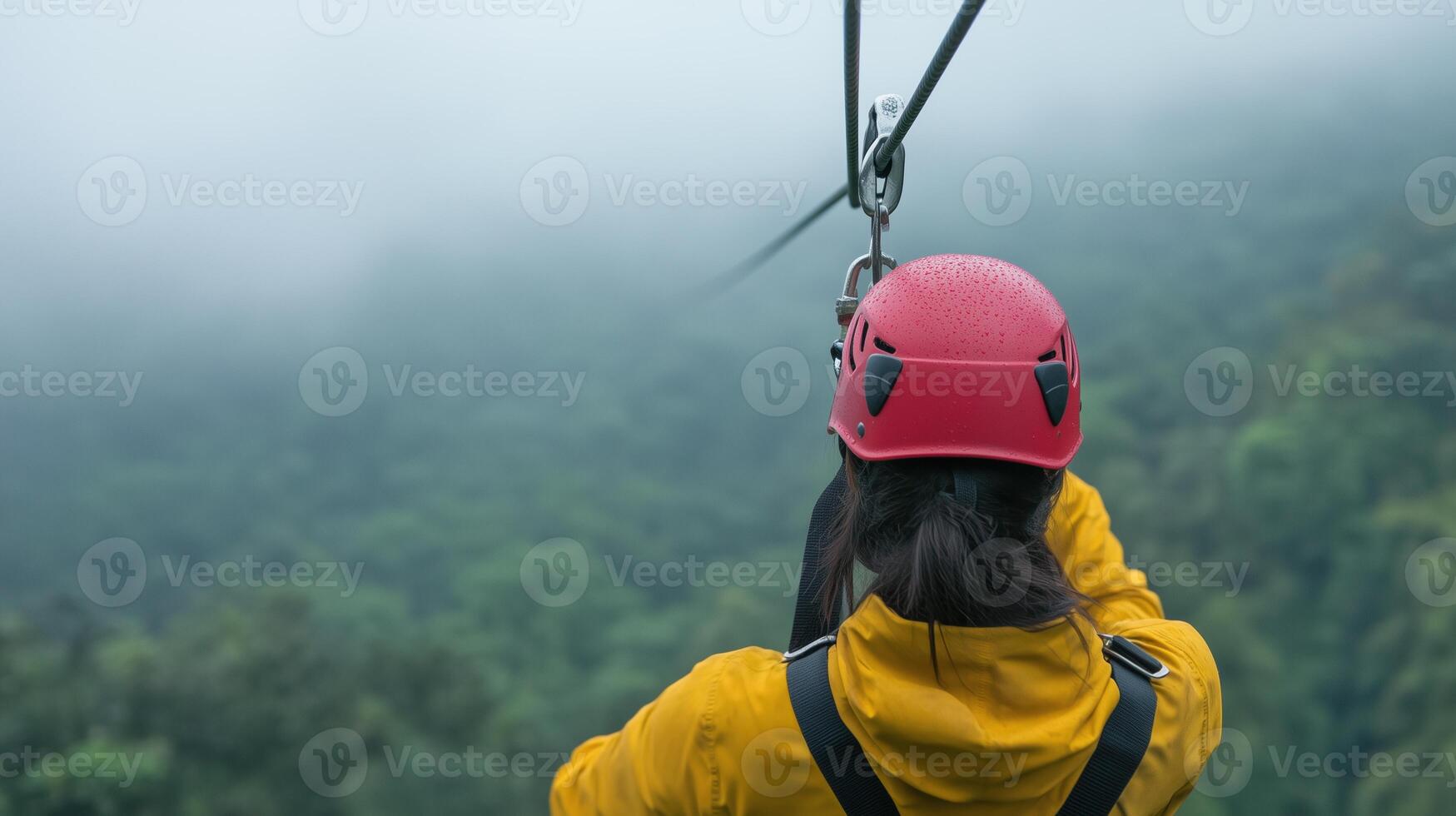 Exciting Zip Lining Adventure Over Misty Costa Rican Jungle with Red Helmet and Yellow Jacket, Perspective from Behind, Thrilling Outdoor Activity Amidst Lush Green Foliage and Dense Fog photo