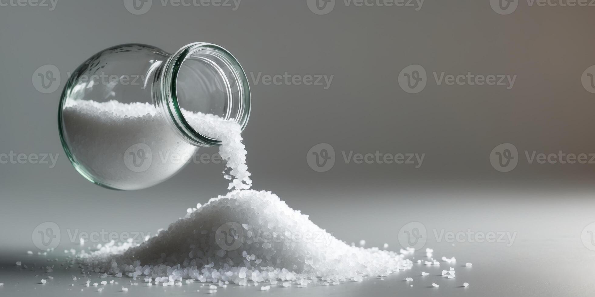 Coarse Salt Pouring from a Glass Jar onto a Light Gray Surface photo