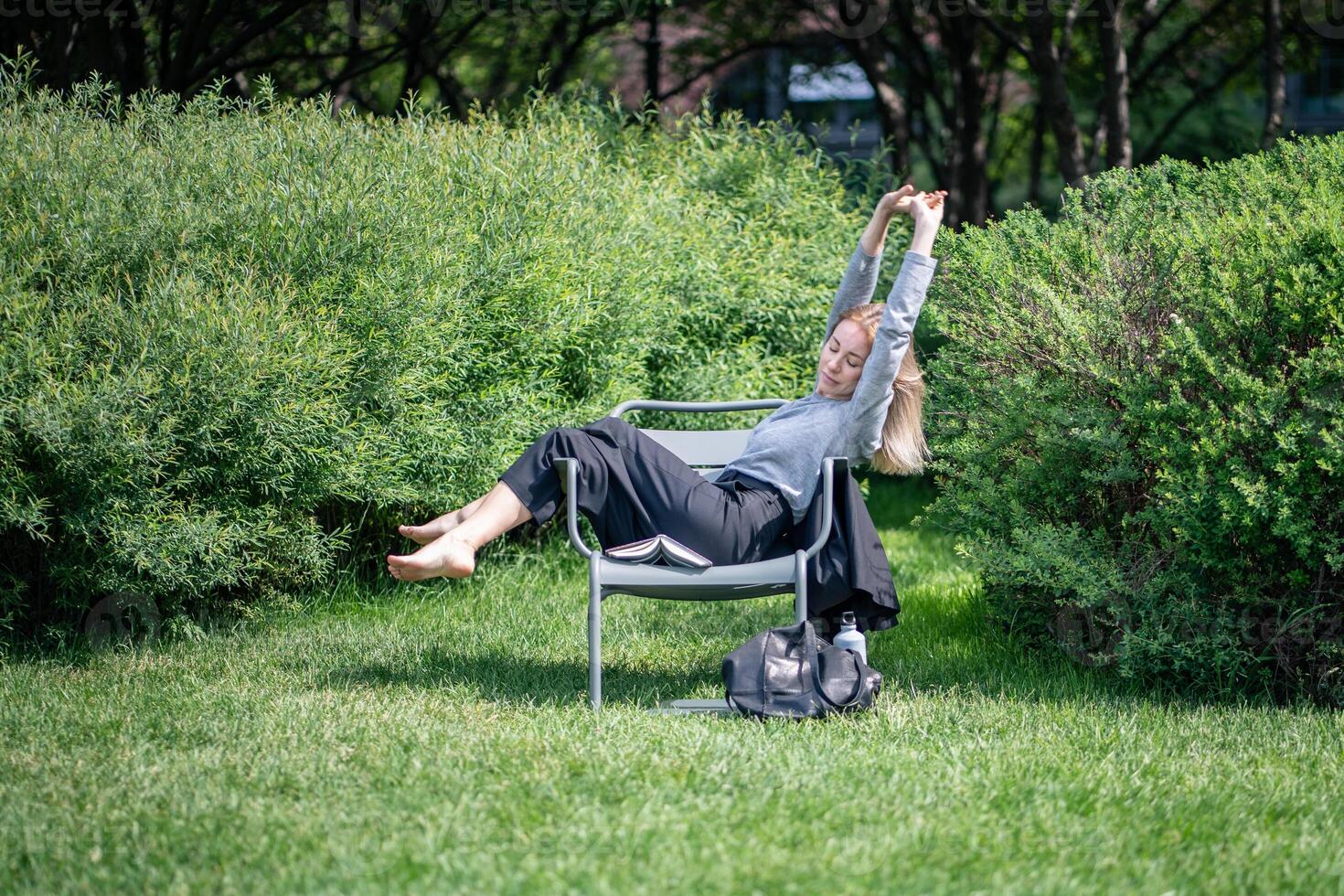 Woman resting, relaxing and stretching while lying on lounge chair in summer green park or garden. photo