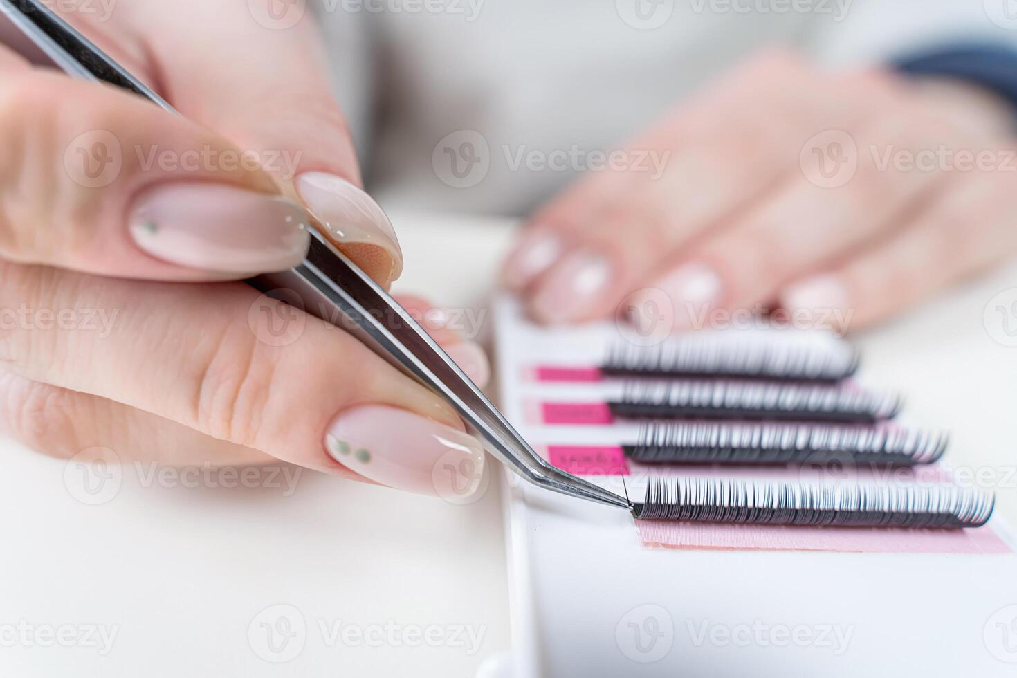 Eyelash Extension Procedure. Close-up of a master at work artificial eyelash extensions material. Hands of the master taking lashes from the set photo