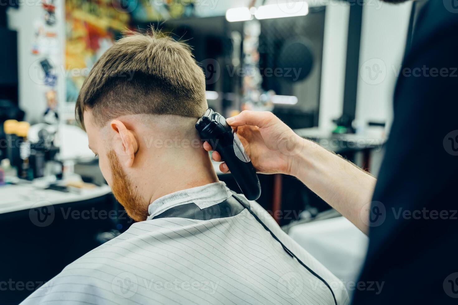 Male haircut with electric razor. Barber makes haircut for client at the barber shop by using hairclipper. Man hairdressing with electric shaver. photo