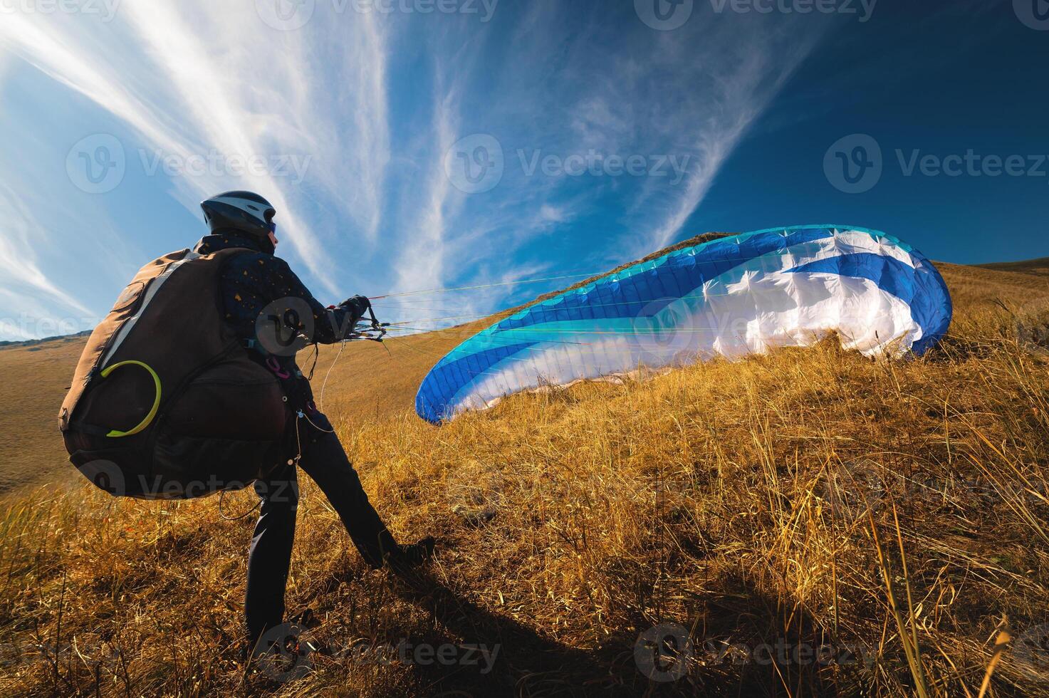 paraglider prepares for a paragliding flight or has already completed it and landed, standing on a hill in the grass, surrounded by a vibrant autumn landscape photo