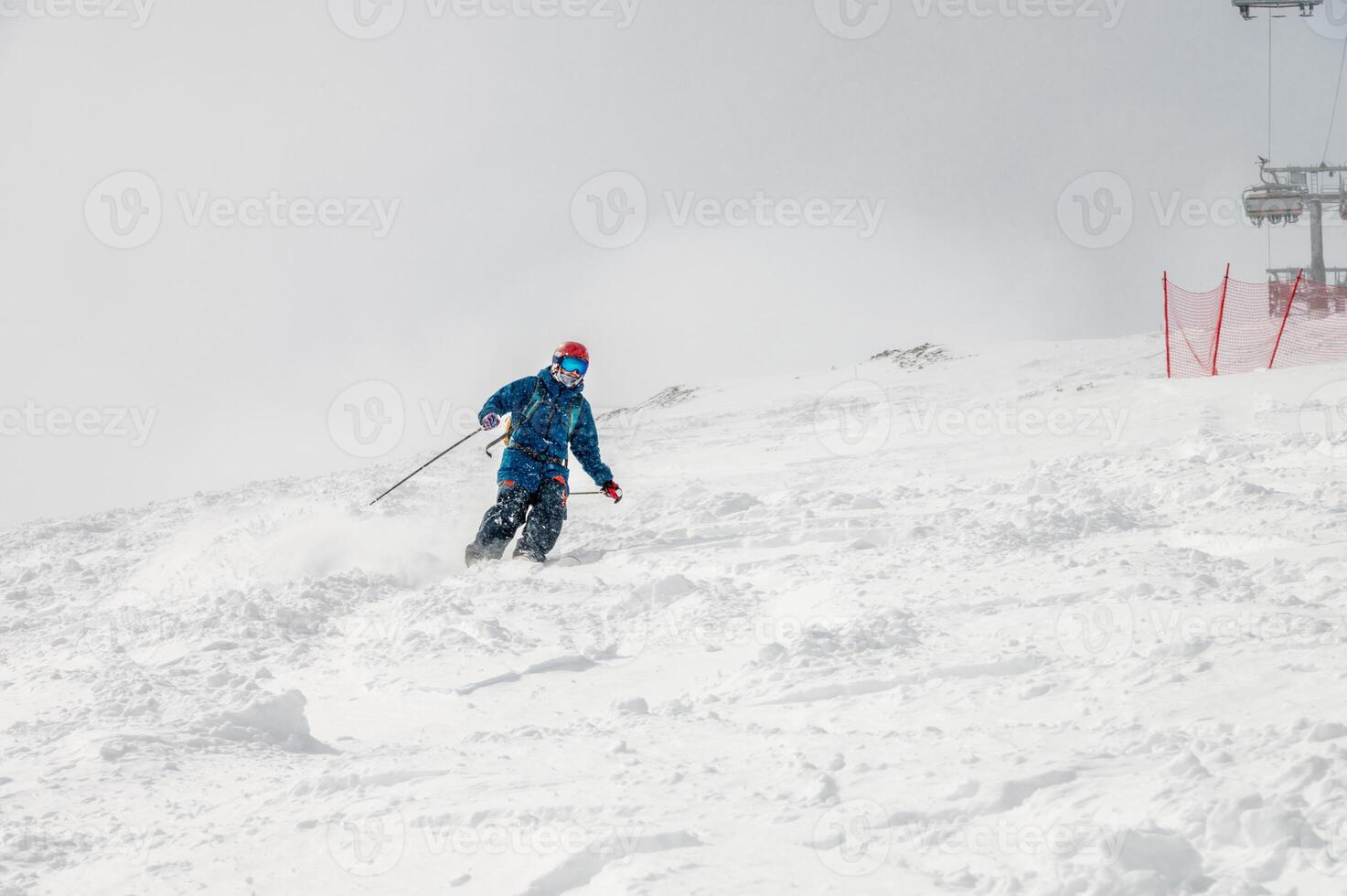 Action photo of a male skier in blue outfit on a slope going down a mountain in the Alps. Active winter recreation, going down a mountain on a cloudy day.