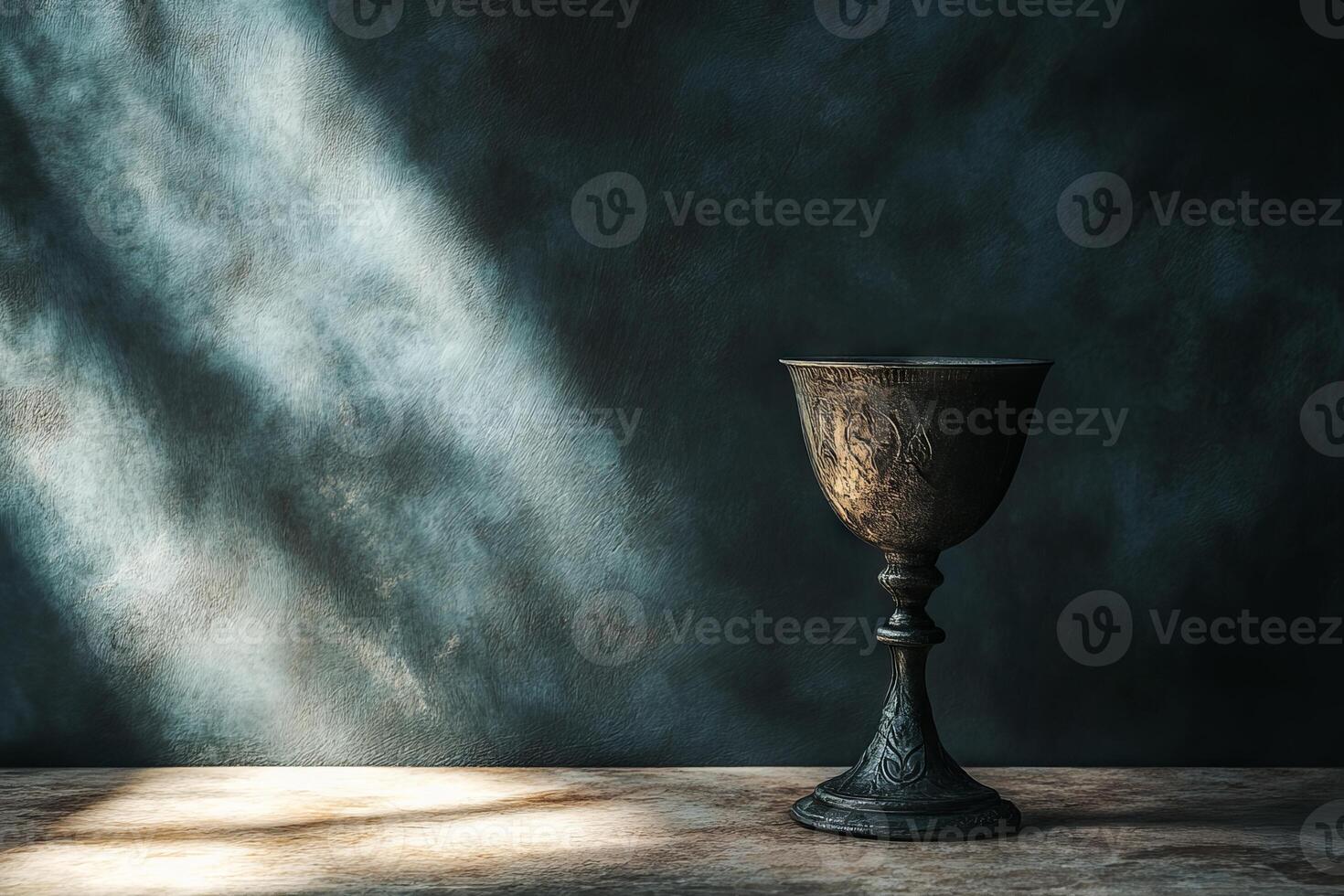 A silver cup sits on a table in front of a wall. The cup is empty and the table is empty photo