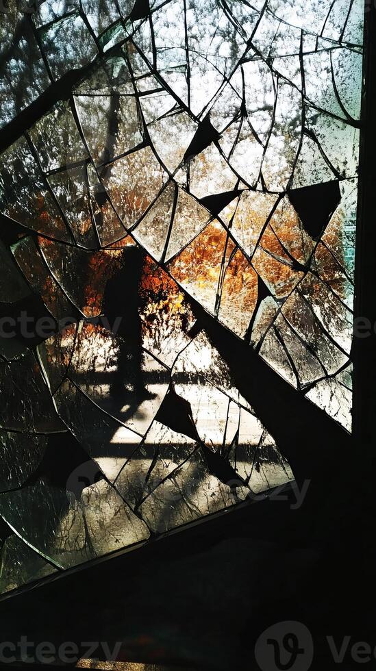 Silhouette of a Person Walking Behind a Broken Glass Window with Sunlight Streaming Through photo